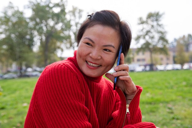 Souriante capitonnée belle femme chinoise parlant au téléphone portable au parc