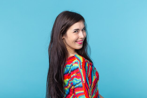 Souriante charmante jeune femme brune debout contre un mur bleu avec espace de copie.