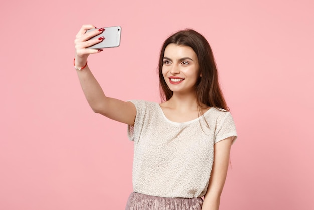 Souriante charmante jeune femme dans des vêtements légers décontractés posant isolé sur un portrait de studio de fond de mur rose pastel. Concept de style de vie des gens. Maquette de l'espace de copie. Faire selfie tourné sur téléphone mobile.