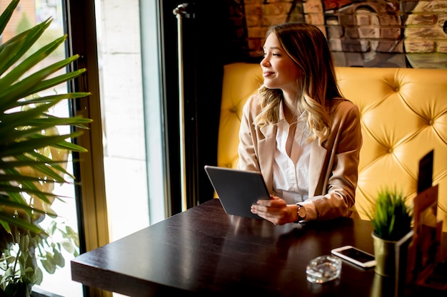 Souriante charmante jeune femme avec tablette numérique au café