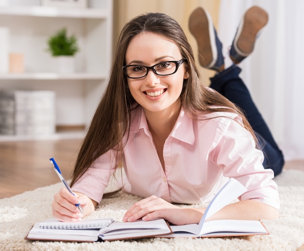 Souriante étudiante lit des livres à la maison.