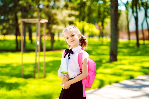 Souriante étudiante portant sac à dos scolaire et tenant le cahier d'exercices. Portrait d'une fillette caucasienne heureuse en dehors de l'école primaire. Écolière souriante