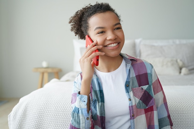 Souriante jeune adolescente afro-américaine faisant un appel téléphonique parlant avec un ami dans la chambre à la maison