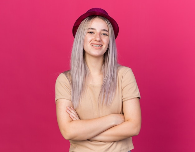 Souriante jeune belle fille portant un chapeau de fête avec des appareils dentaires croisant les mains