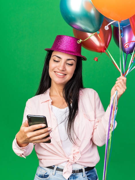 Souriante jeune belle fille portant un chapeau de fête tenant des ballons prendre un selfie