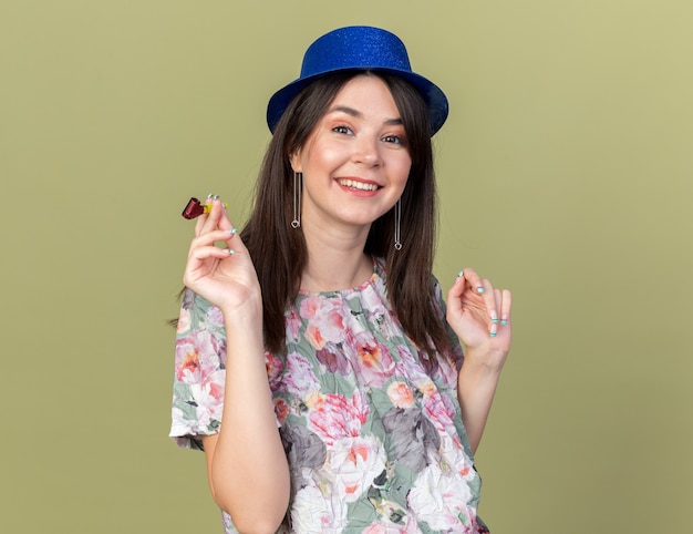 Souriante jeune belle fille portant un chapeau de fête tenant un sifflet de fête