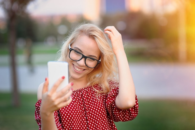 Souriante jeune blogueuse à lunettes avec le téléphone dans le parc de l'été