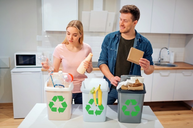 Souriante jeune famille mettant du plastique, du papier et d'autres déchets dans des poubelles bio dans la cuisine