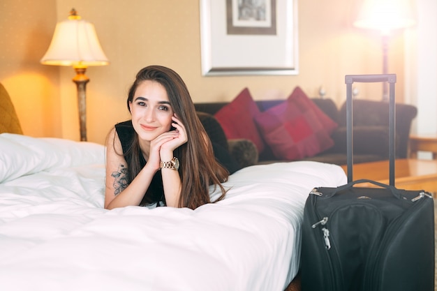 Souriante jeune femme d'affaires au lit, fille lèche sur le lit près de la valise.