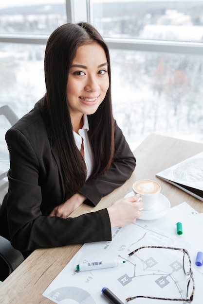 Souriante jeune femme d'affaires, boire du café à la table de bureau