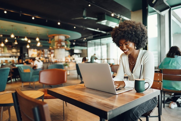 Souriante jeune femme africaine assise avec un ordinateur portable au café