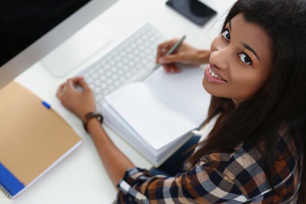 Souriante jeune femme afro-américaine sur un appareil de luxe à journal ouvert en milieu de travail sur le lieu de travail