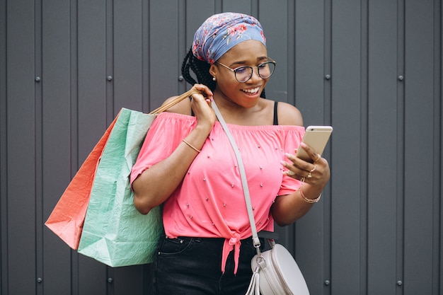 Souriante jeune femme afro-américaine tenant le téléphone et les sacs à provisions