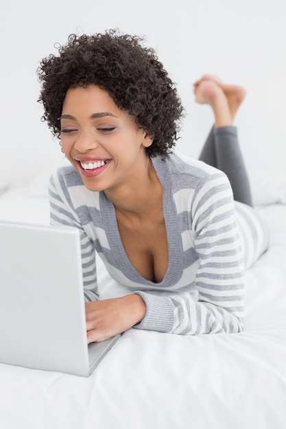 Souriante jeune femme à l&#39;aide d&#39;ordinateur portable au lit