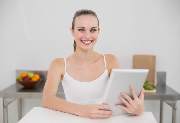 Souriante jeune femme à l&#39;aide de son tablet pc en regardant la caméra