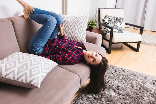Souriante jeune femme allongée sur le canapé dans le salon