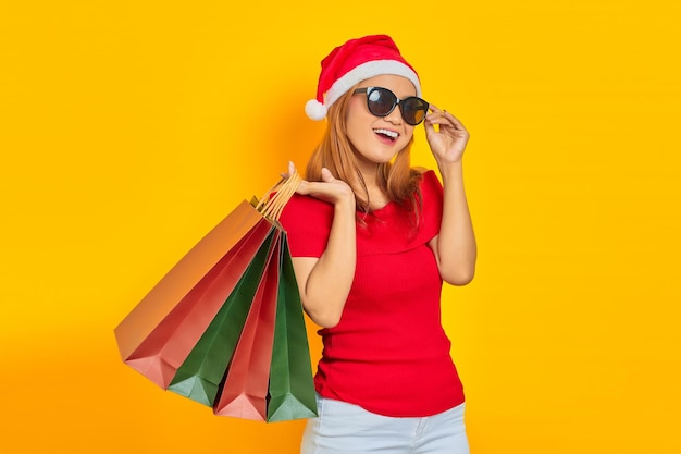 Souriante jeune femme asiatique en chapeau de père Noël et lunettes de soleil tenant des sacs à provisions