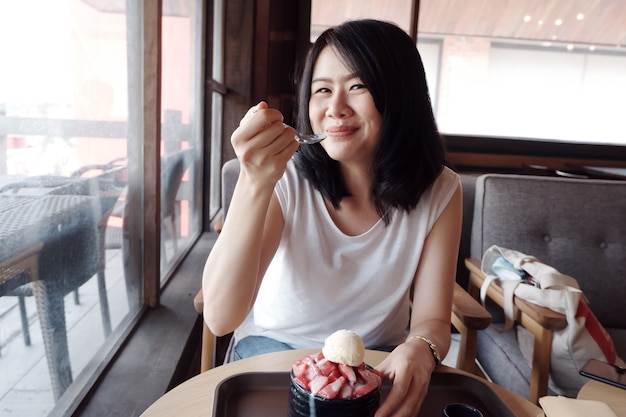 Souriante jeune femme asiatique heureuse avec un délicieux Bingsu aux fraises au café. Mode de vie et temps de détente d'une femme d'affaires sur le concept de vacances