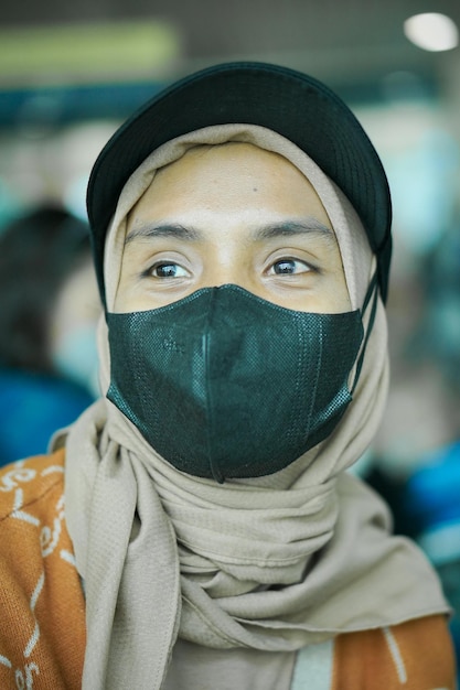 Souriante jeune femme asiatique en hijab portant un masque et un chapeau assis dans la salle d'attente