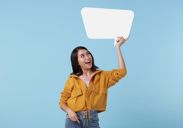 Souriante jeune femme asiatique montrant une bulle vide sur fond de studio bleu