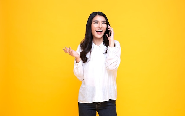 Souriante jeune femme asiatique occasionnelle parlant de téléphone intelligent isolé sur fond jaune.