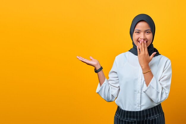 Souriante jeune femme asiatique présentant le produit et regardant la caméra sur fond jaune