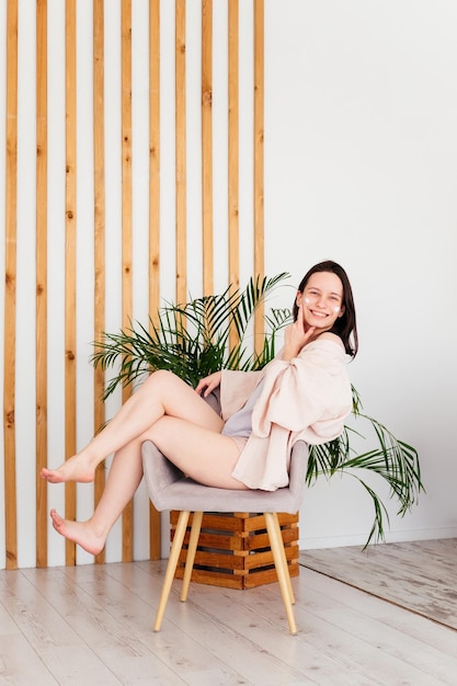 Photo souriante jeune femme assise sur une chaise appliquant de la crème sur le visage à la maison concept de soins de la peau de routine de beauté