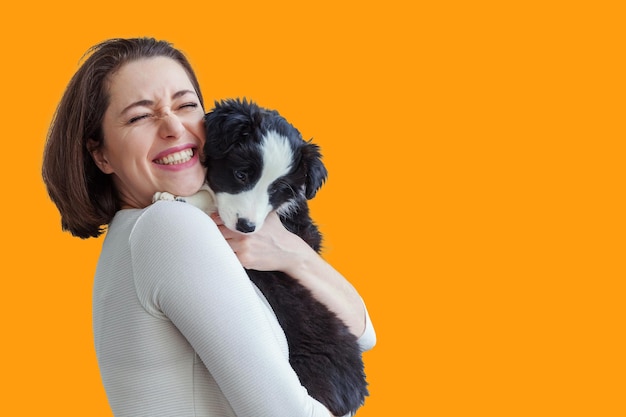 Souriante jeune femme attrayante embrassant un mignon chiot chien border collie isolé sur fond jaune Fille embrassant un nouveau membre charmant de la famille Soins pour animaux de compagnie compagnon chien ami concept