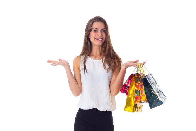 Souriante jeune femme aux cheveux longs en blouse blanche et jupe noire tenant des sacs à provisions en studio