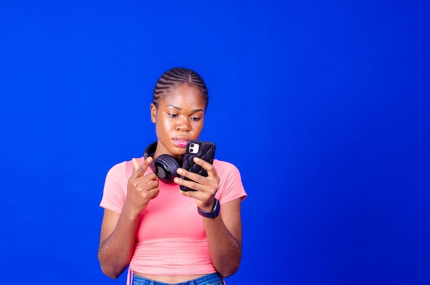 Souriante jeune femme ayant du succès tenant un téléphone portable sur fond de studio bleu