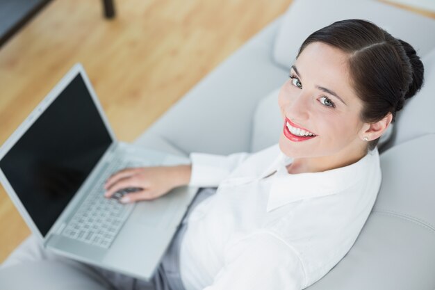 Souriante jeune femme bien habillée à l&#39;aide d&#39;un ordinateur portable sur le canapé