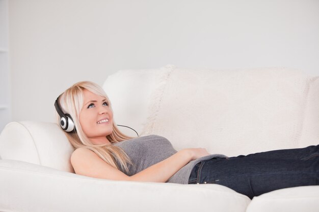 Souriante jeune femme blonde avec un casque allongé dans un canapé