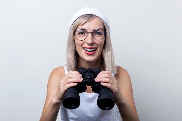 Souriante jeune femme blonde avec des jumelles sur un fond clair