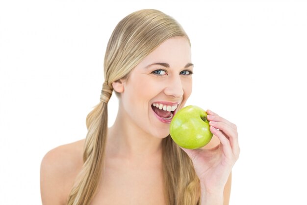 Souriante jeune femme blonde mange une pomme