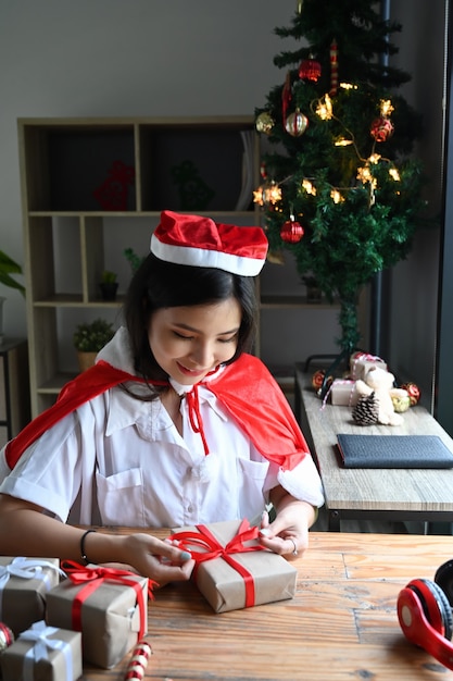Souriante jeune femme en bonnet de Noel décorant des cadeaux de Noël dans le salon.