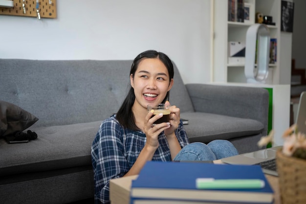 Souriante jeune femme buvant du café assise dans le salon