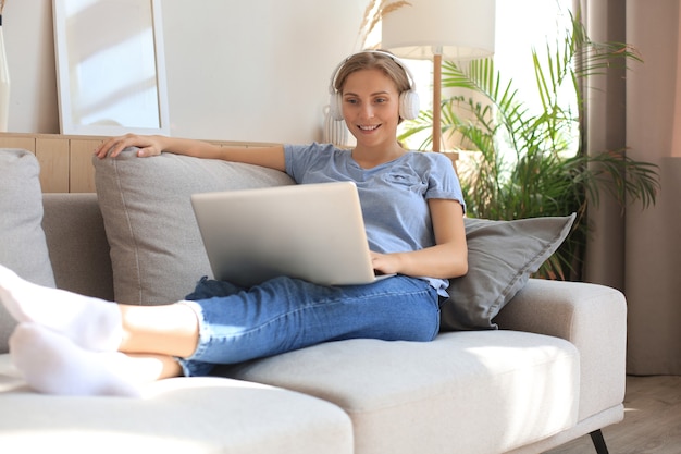 Souriante jeune femme avec un casque et un ordinateur portable sur le canapé.