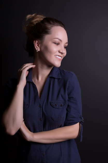 Souriante jeune femme dans des vêtements à la mode, posant sur un fond de studio sombre