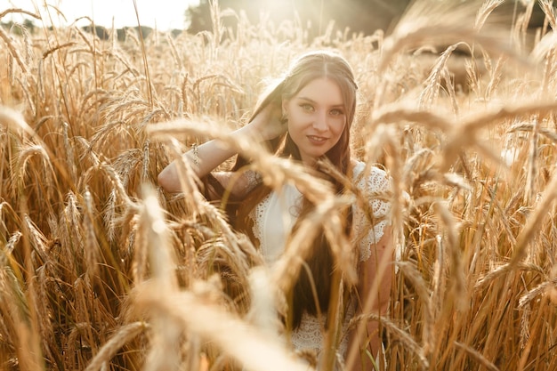 Souriante jeune femme debout dans un champ de blé doré en été et regardant la caméra