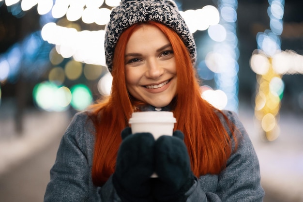 Souriante jeune femme dégustant une tasse de café à l'extérieur