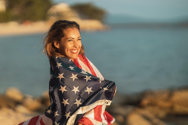 Souriante jeune femme avec drapeau national américain profitant d'une journée de détente sur la plage.