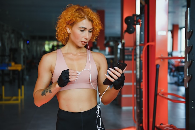 Souriante jeune femme avec des écouteurs à l'aide de smartphone dans la salle de sport