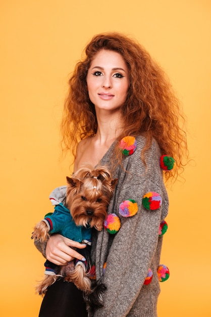 Souriante jeune femme étreignant un chien isolé sur mur orange