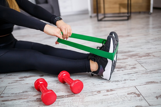 Souriante jeune femme exerçant avec une bande élastique à l'entraînement de remise en forme à domicile. Concept de mode de vie sain. Faire du sport à la maison pendant le confinement