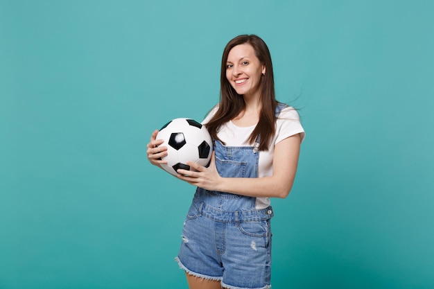 Souriante jeune femme fan de football soutient l'équipe préférée tenant un ballon de football isolé sur fond bleu turquoise en studio. Émotions des gens, concept de mode de vie de loisirs familiaux sportifs. Maquette de l'espace de copie.