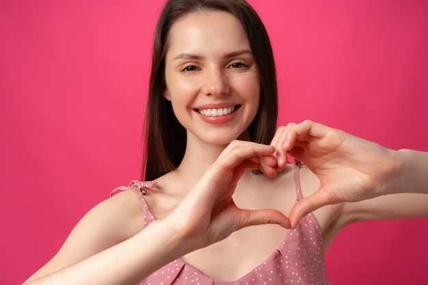 Souriante jeune femme gesticulant signe de coeur avec les mains montrant l'amour