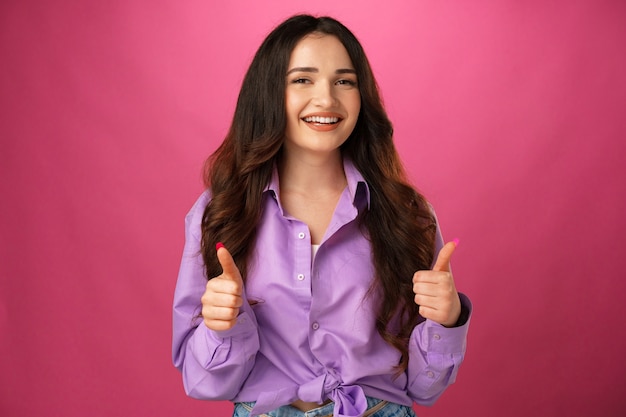 Souriante jeune femme heureuse montrant les pouces vers le haut sur fond rose