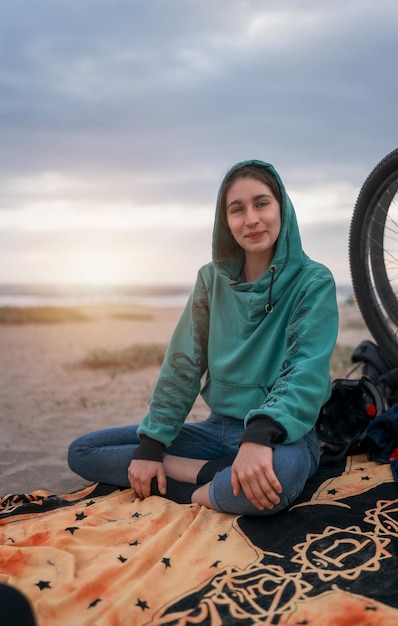 Souriante jeune femme latine assise sur la plage à l'extérieur à côté d'un vélo portraitx9