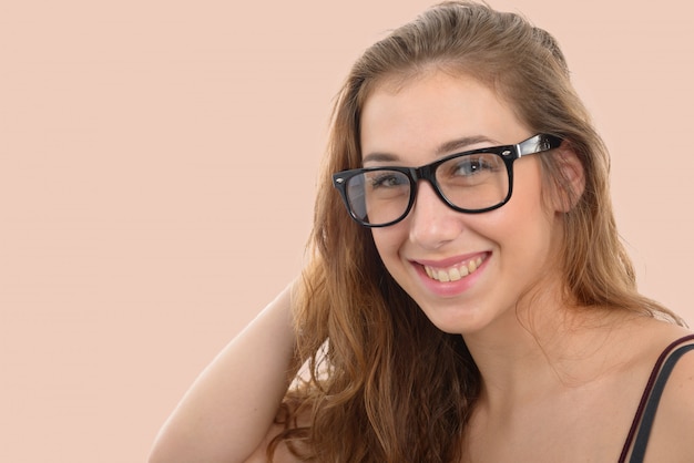 Souriante jeune femme avec des lunettes noires, sur fond rose clair