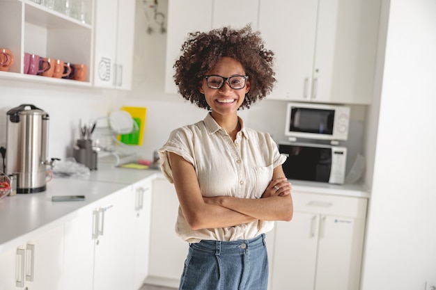 Souriante jeune femme à lunettes posant sur la cuisine de coworking